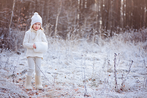 cute child girl in white outfit walking in winter snowy forest