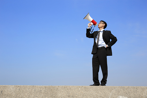 happy business man using megaphone shouting with blue sky background, asian