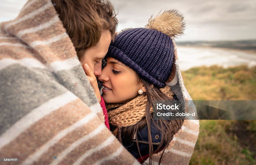 Young couple embracing outdoors under blanket in a cold day Closeup of young beautiful couple embracing under blanket in a cold day with sea and dark cloudy sky on the background 2015 Stock Photo