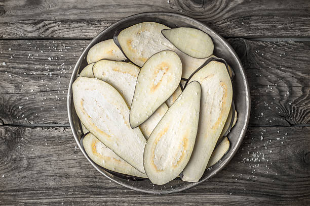 Sliced eggplants with salt in metal plate on  wooden table