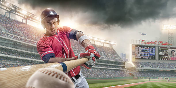 Baseball Player Batting Ball in Close Up In Baseball Arena An extreme close up image of professional male baseball player in red uniform, just about to make contact and hit baseball. The action takes place during a baseball game in a generic outdoor floodlit stadium full of spectators under a dramatic stormy evening sky. The location is fake.  baseball player stock pictures, royalty-free photos & images