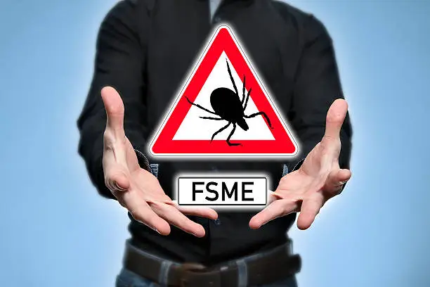 Doctor pointing to a sign with a tick and FSME (in german for TBE)