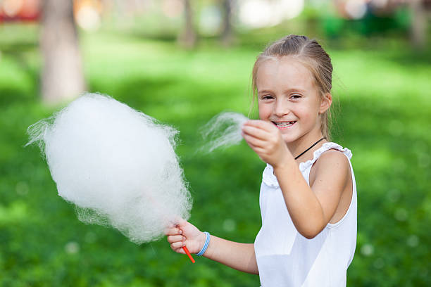 Cute girl with white cotton candy Cute girl with white cotton candy in the summer park child cotton candy stock pictures, royalty-free photos & images