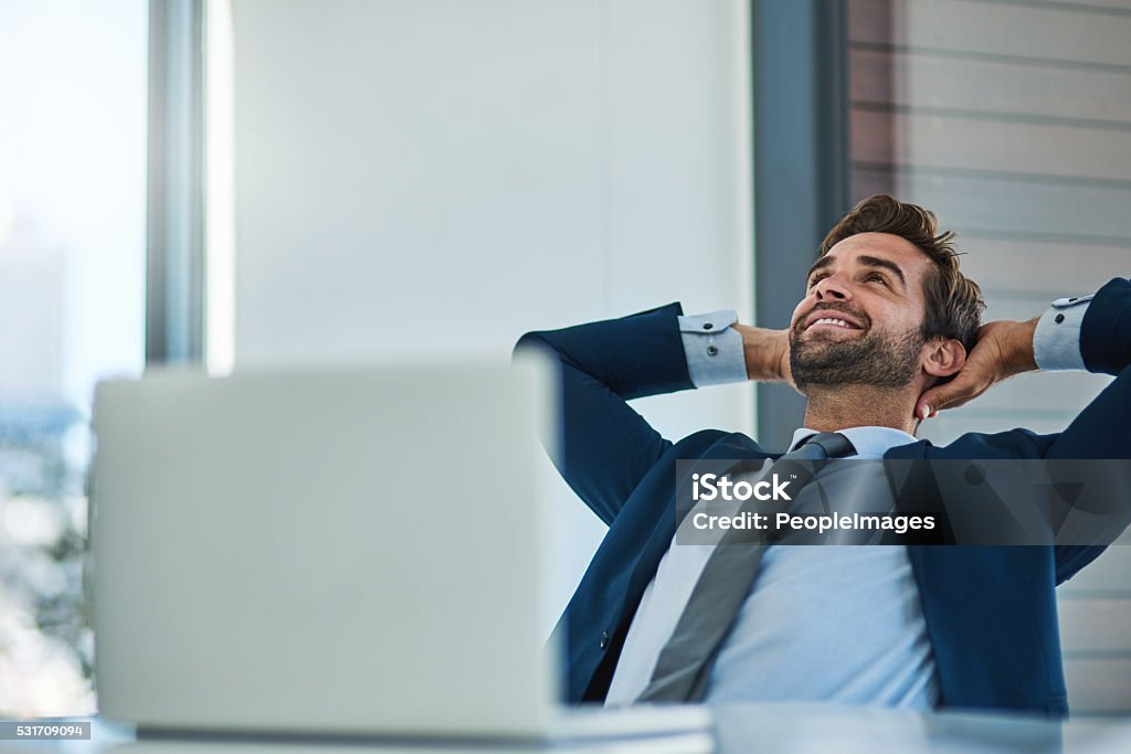 Things are finally going my way Shot of a young corporate businessman taking a break at an office desk Businessman Stock Photo