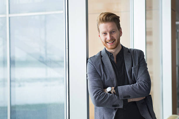 istock Smiling young  businessman leaning against window in office hallway. 531711428