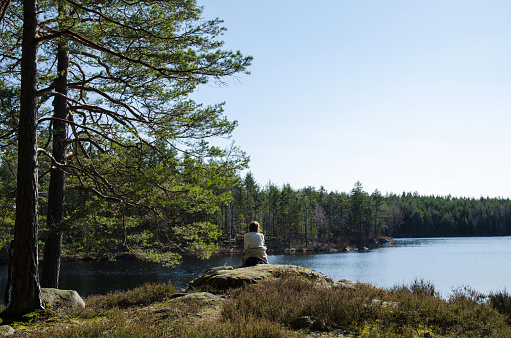Woman watching at a lake in the woodlands of the province Smaland in Sweden