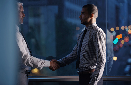 Cropped shot of two businessmen shaking hands in an office setting at night