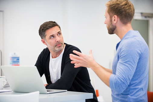 Mid adult businessman discussing over laptop with male colleague at desk in office