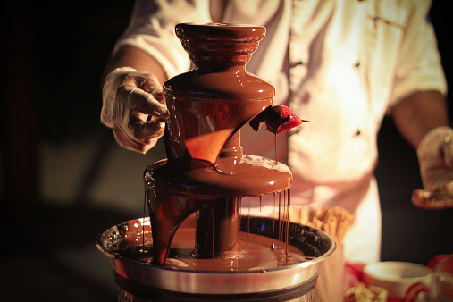 Chef is preparing a strawberry skewer under a chocolate fountain/ Schokoladenbrunnen