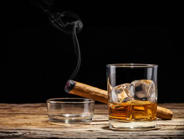 Whiskey drink with smoking cigar on wooden table