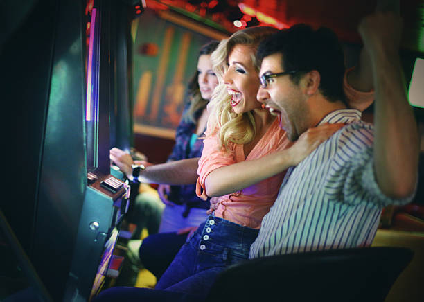 Casino night. Group of young adults in mid 20's playing slots in a casino,winning and having fun.They have just won and are celebrating and screaming.Excited happy people.Many slot machines and people in background,out of focus. coin operated stock pictures, royalty-free photos & images