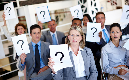 Shot of a group of businesspeople holding up signs with question marks on them during a work presentation