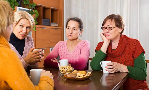 sad senior female friends drinking coffee and sharing problems at table
