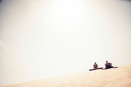 tourists standing at the top of a dune, getting ready for some sandboarding fun