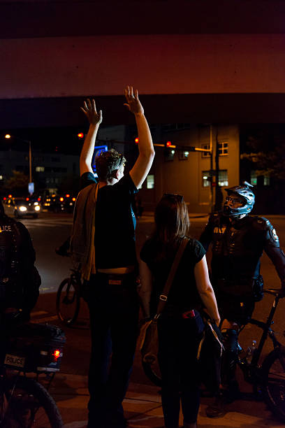 Anarchists Seattle, USA - May 1, 2016: A protestor holding his hands in the air as Seattle Police officers in riot gear on 4th avenue direct them to stay on the sidewalk as they make their way back into the city after the Anti-Capitalist Protest early in the night. german social democratic party photos stock pictures, royalty-free photos & images
