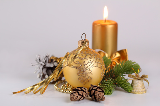 Christmas card with  natural pinecones, burning golden candle, golden ball, green paw of the New Year's tree, white background.