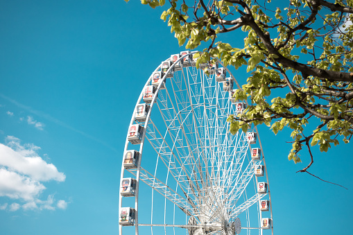 Paris, France - May 3, 2016: Detail of ferris wheel (with EURO 2016 faces) at Place de la Concorde in Paris. View from below the green tree. Blue sky with white clouds in the background.