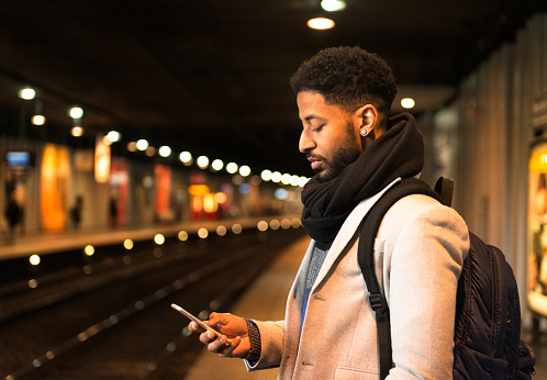 A man checking his phone as he waits for a subway train at a Paris Metro station.