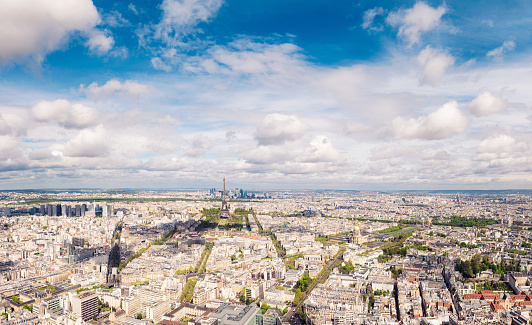 A panoramic format, high angle view over the city of Paris in spring, with the Eiffel Tower near the centre of the image, and the La Defence business district behind it.