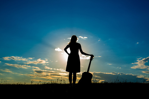 Silhouette woman playing guitar in the sunset