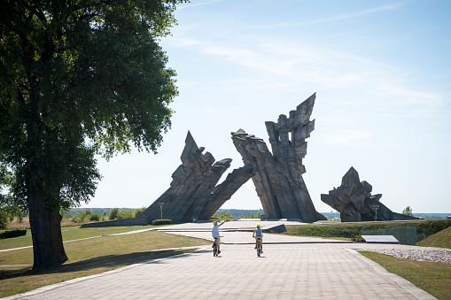 Kaunas, Lithuania - August 15, 2015: Two boys ride bicycles at the Ninth Fort in Kaunas, Lithuania. Beyond the boys, other people walk at the base of the 105-foot (32-meter) high memorial to the victims of Nazism, which was erected in 1984. The fort was used as a place of execution for Jews, captured Soviets, and others.