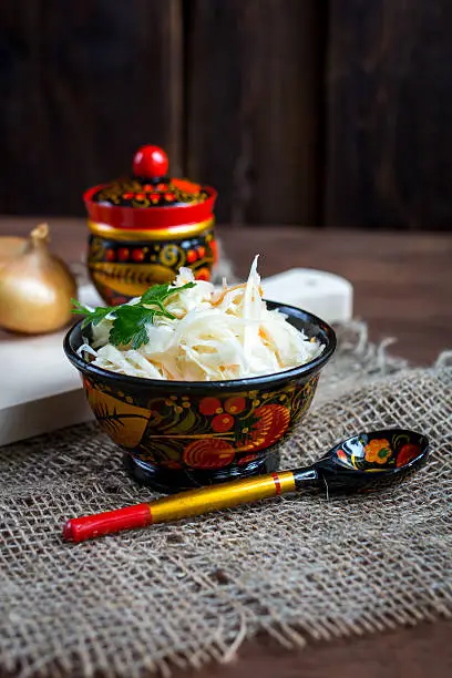 Sauerkraut with carrot in wooden bowl on dark wooden background. Rustic style. Selective focus.
