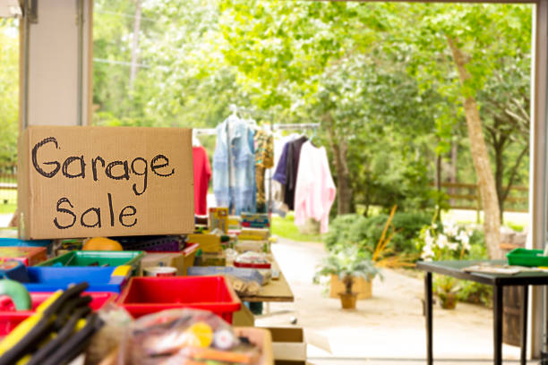 Consumerism: Garage sale sign posted in suburbs. Open for business. Home garage, yard sale in summer season. Tables set up with many rows of discarded household items. 