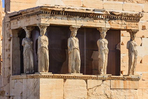 Architectural Detail of the Karyatids porch, so named after the six statues of Korae (maidens), who appear to support the roof of the porch with their heads; it is part of the Erechtheion temple situated to the north of the Parthenon at the Acropolis. Close-up photo shot in the morning sunlight; horizontal format. Focus on third pillar from left. No people.