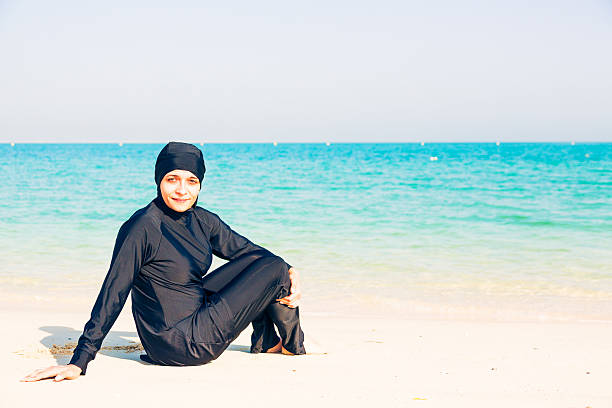 young woman wearing burkini sitting by the beach - 回教泳裝 圖片 個照片及圖片檔