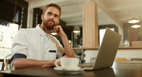 Shot of a young man sitting in front of a laptop in a cafe