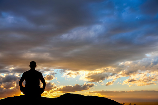 yoga man silhouette sitting in lotus position watching the sunset sky, sandia mountains, albuquerque, new mexico, horizontal, copy space.