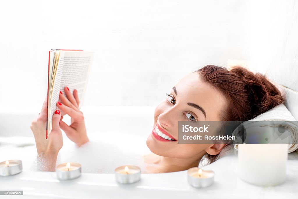 Woman bathing Young woman reading book while lying in the bath with foam and candles 2015 Stock Photo