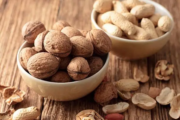 Photo of Heap of walnuts in a bowl and broken shells around