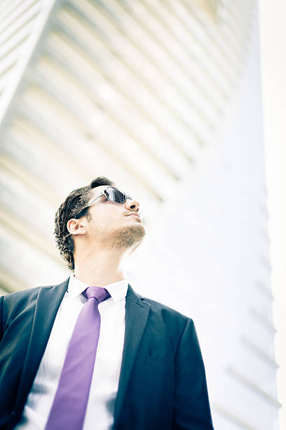 Young businessman wearing a red tie gazes confidently at the city skyline, contemplating his next strategic move amidst the vibrant energy of the bustling urban landscape