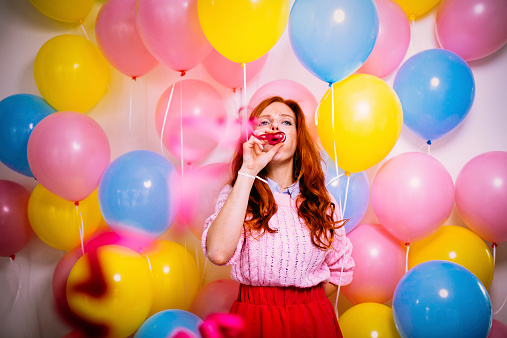 Young woman blows streamers whilst standing in front of a balloon wall