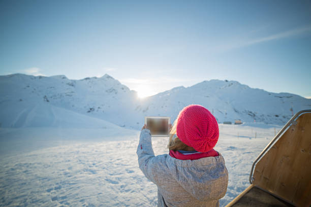 Woman on snow capped alps takes picture using digital tablet Young woman at the top of the ski runs taking a picture of the snow capped alps with a digital tablet.Switzerland. switzerland european alps ski winter stock pictures, royalty-free photos & images