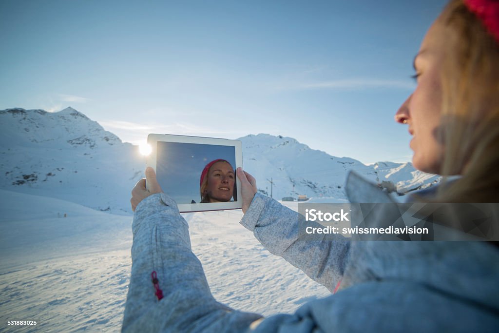 Woman on ski runs taking picture with digital tablet Young woman at the top of the ski runs taking a picture of the snow capped alps with a digital tablet.Switzerland. 2015 Stock Photo