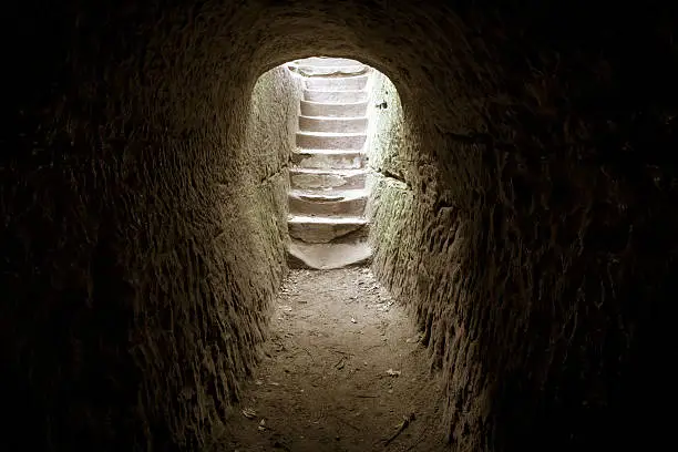 Light at the end of the tunnel. Dark stone room with a stairway encased in sunlight.