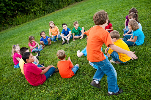 Color photo of a group of boys and girls sitting in a circle and playing a game of \