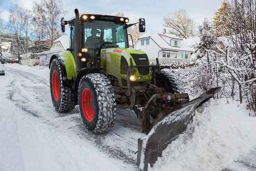 Oslo, Norway - January 10, 2015. Mature man driving a tractor with a snow plow to clear the streets for snow