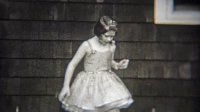 1936: Confident ballet girl solo dancing in front of house.