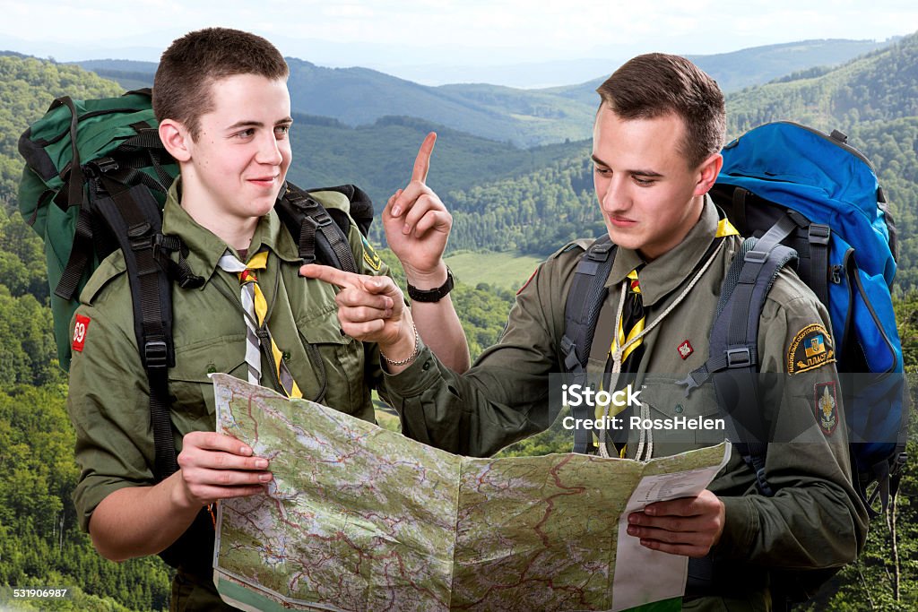 Scout tour Two young scout boys with backpacks holding the map and showing the right way traveling in the mountains Boy Scout Stock Photo