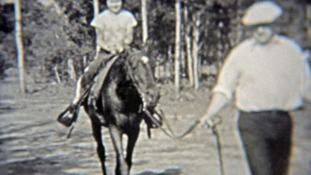 1937: Girl getting horse riding lessons through the forest.