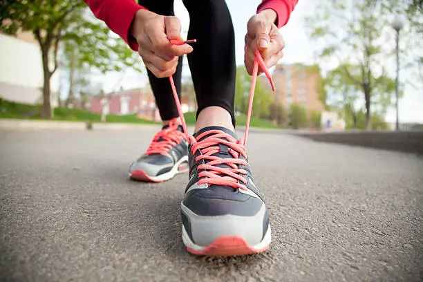 Sporty woman tying shoelace on running shoes before practice. Female athlete preparing for jogging outdoors. Runner getting ready for training. Sport active lifestyle concept. Close-up