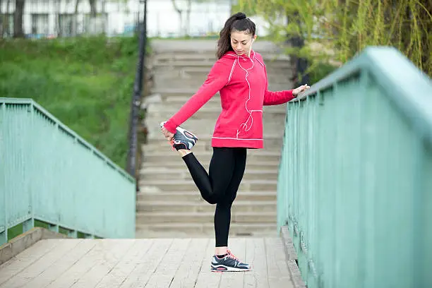 Portrait of sporty woman doing stretching workout in park before jogging. Female athlete runner getting ready for running routine on the bridge. Sport active lifestyle concept. Full length