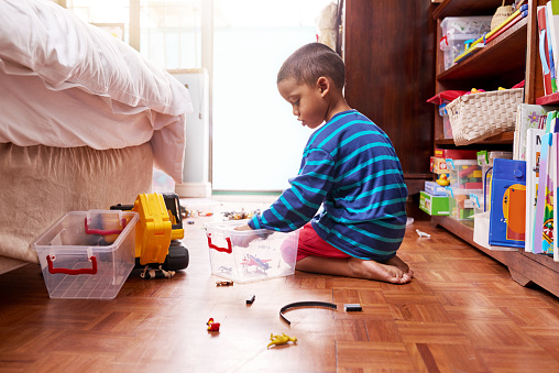 Shot of a young boy sitting on the floor with toys in a bedroom