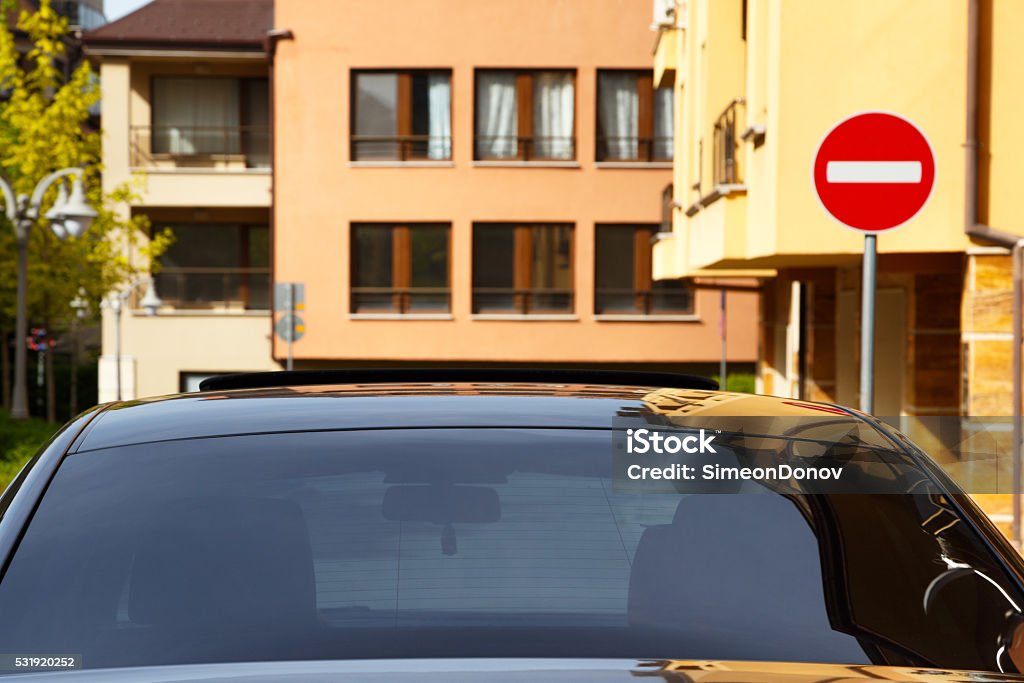 Car with dark tinted windows Car with dark tinted windows in an urban street below colorful apartment blocks and a no entry sign, close up view of the windshield Car Stock Photo