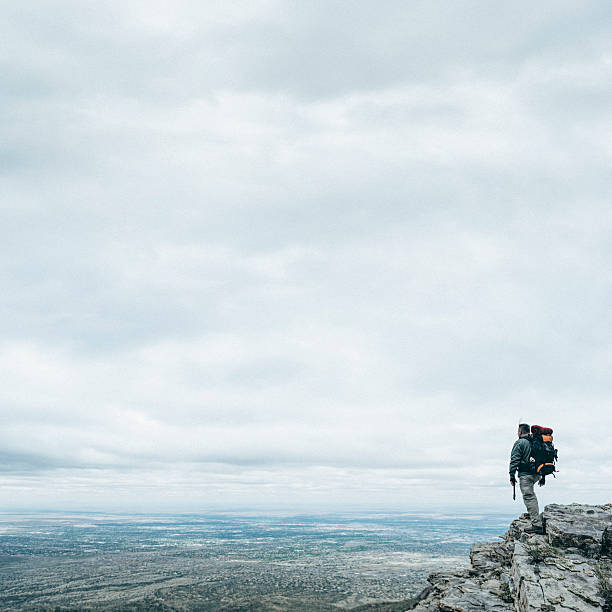 A lone hiker stands on the edge of the cliff in Caucasus, overlooking a vast valley and blue sky. High quality photo