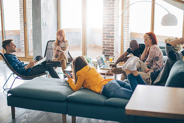 Working and playing under one roof Group of young people spending their time in common living room. Checking their gadgets to catch up with latest news or messages. They are friends who sharing living space. roommate stock pictures, royalty-free photos & images