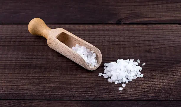 salt with wooden spoon and glass saltshaker on wooden background